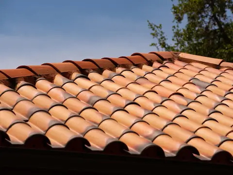 Two-piece clay barrel tiles on a low-pitched roof, with mortar-set ridge tiles along the top and blue sky behind
