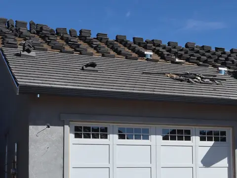 Flat gray concrete roof tiles laid in straight courses on the lower half of a roof, with stacks of tiles waiting on the upper half