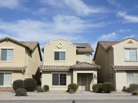 Three two-story stucco houses with tile roofs on a residential street, with gravel yards and desert shrubs in front
