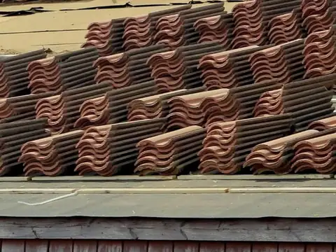 Concrete roof tiles lifted and stacked in rows on a roof, with strips of the old underlayment exposed between the stacks and along the eave
