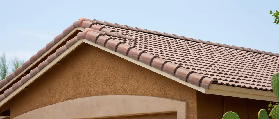 A concrete S-tile roof on the gable of a tan stucco garage, with a prickly pear cactus in the foreground